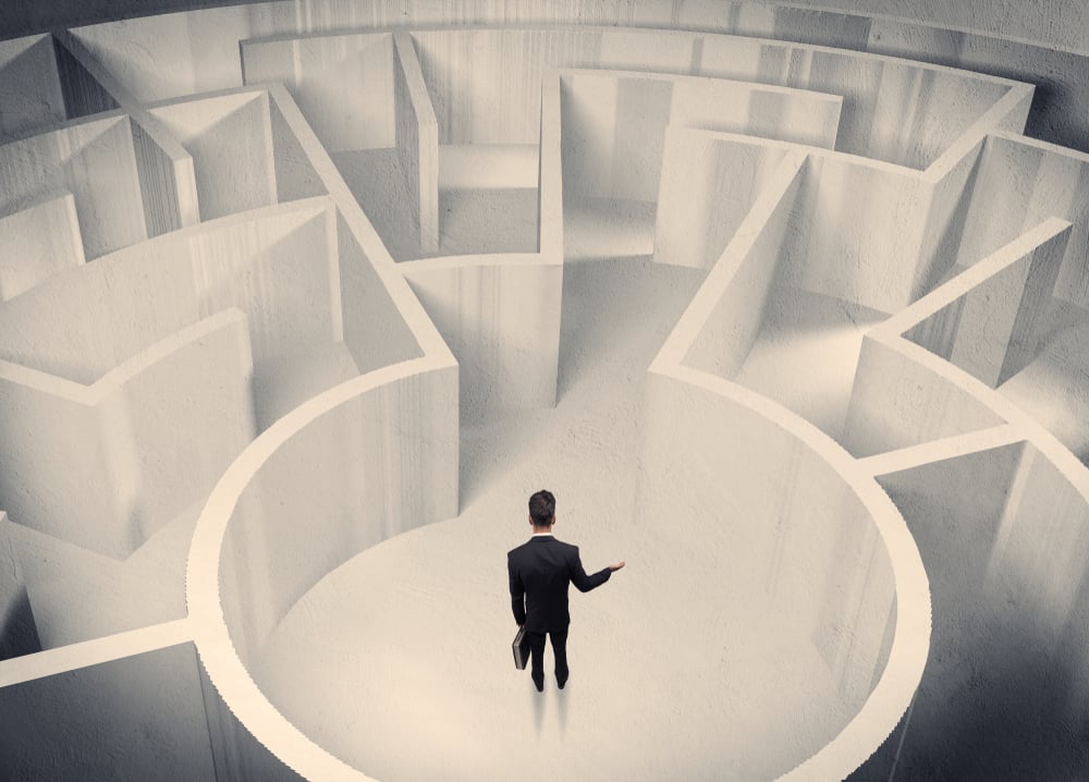 A confused businessman standing in the center of a maze surrounded with walls of the labyrinth